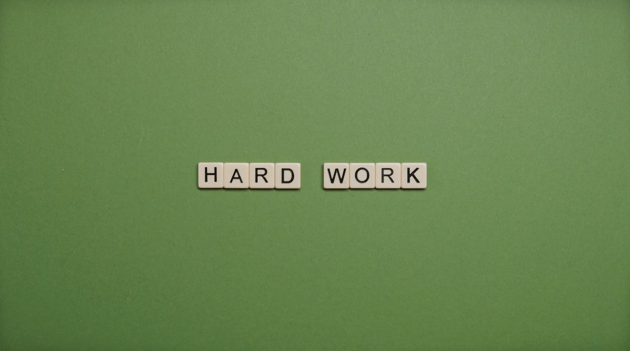 journey Tiles spelling 'hard work' on a green background symbolizing diligence and effort.